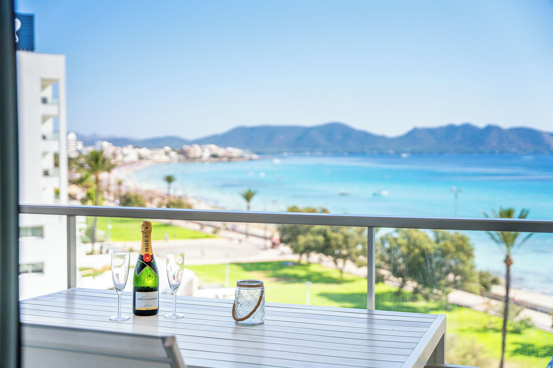 Un balcon avec une bouteille de champagne Moët & Chandon, deux verres et un bocal en verre sur une table donnant sur un paysage côtier.