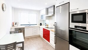 Uma cozinha moderna com eletrodomésticos de aço inoxidável, bancada branca e armários vermelhos.