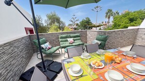 Um terraço ao ar livre com uma mesa posta para o café da manhã, incluindo pratos, xícaras e um copo de suco de laranja.