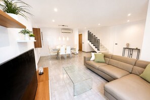 A modern living room with a sofa, a glass coffee table, a TV, and a staircase leading to another level.
