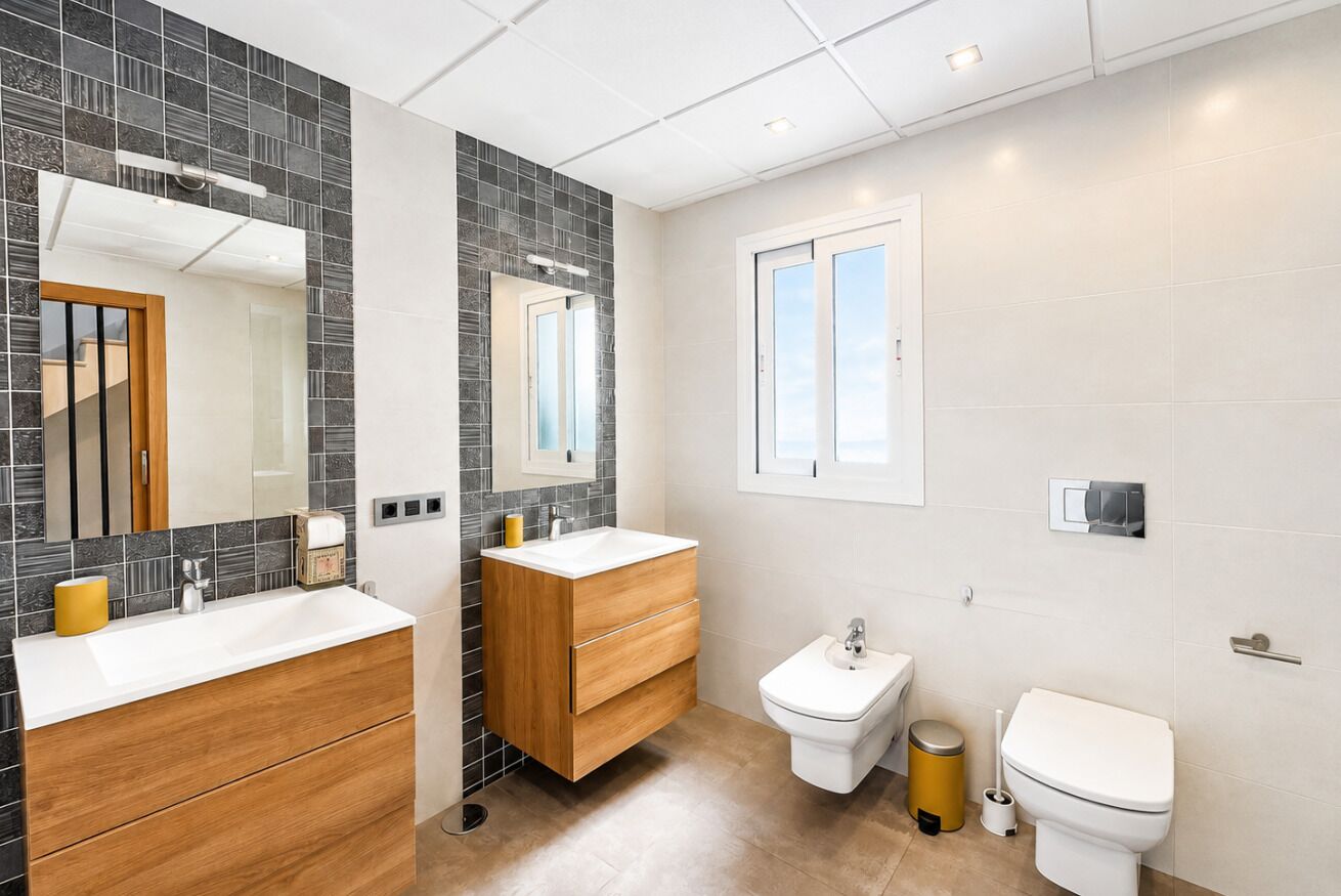 A modern bathroom with a white sink, wooden vanity, a bidet, and a toilet.