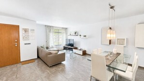 Uma sala de estar moderna com sofá, televisão, mesa de vidro e cadeiras.