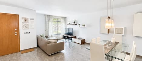 Een moderne woonkamer met een bank, televisie, glazen tafel en stoelen.