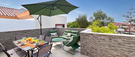 An outdoor patio with a dining table, chairs, and a green umbrella.