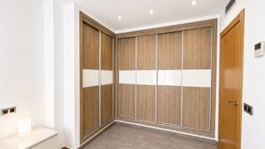 Um quarto com um guarda-roupa de madeira, uma mesa de cabeceira branca e uma porta com puxador.
