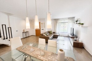 Ein modernes Wohnzimmer mit einem Glastisch, Ledersofas, Pendelleuchten und Blick ins Freie.