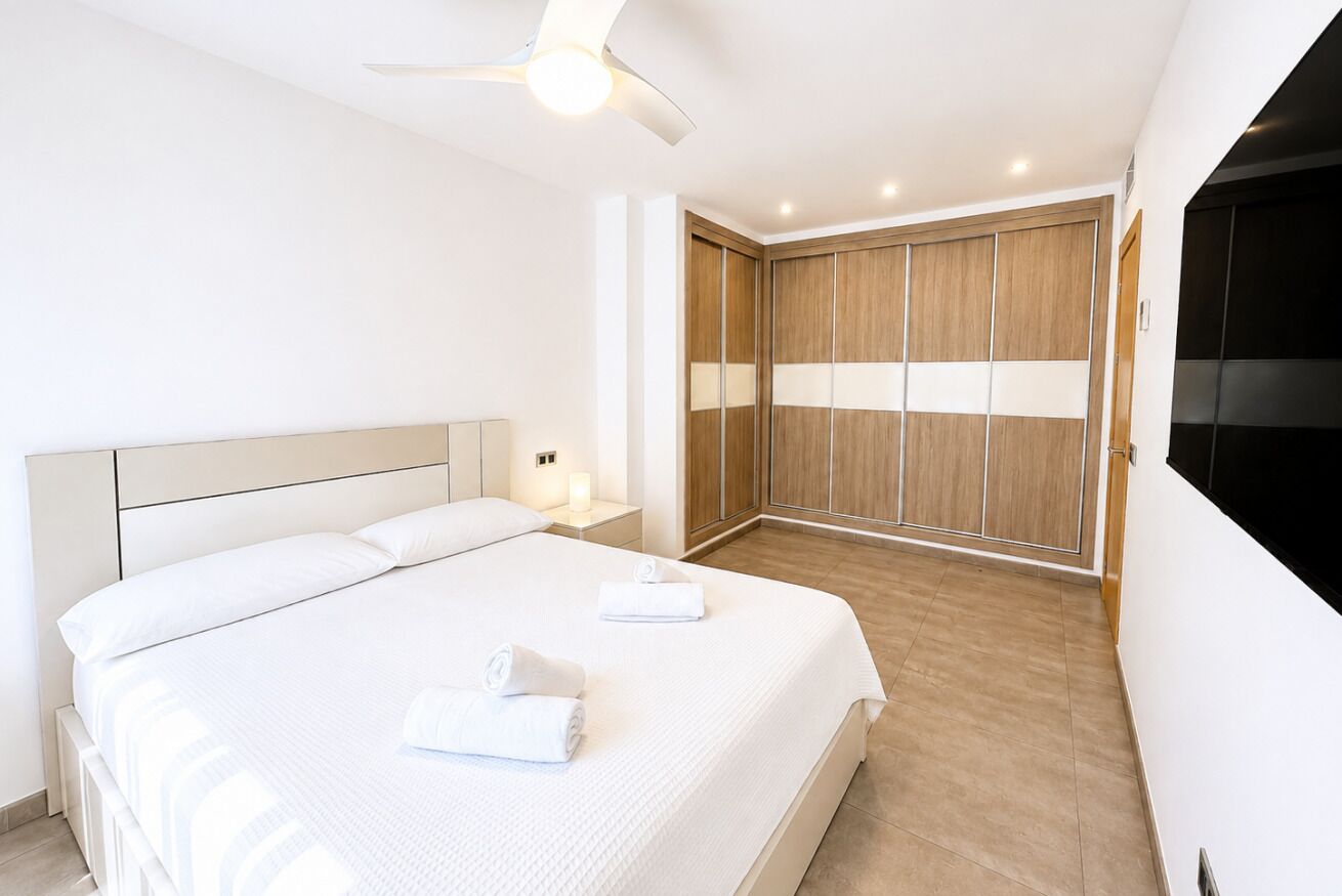 Una habitación de hotel con cama, mesitas de noche, ventilador de techo y armario.