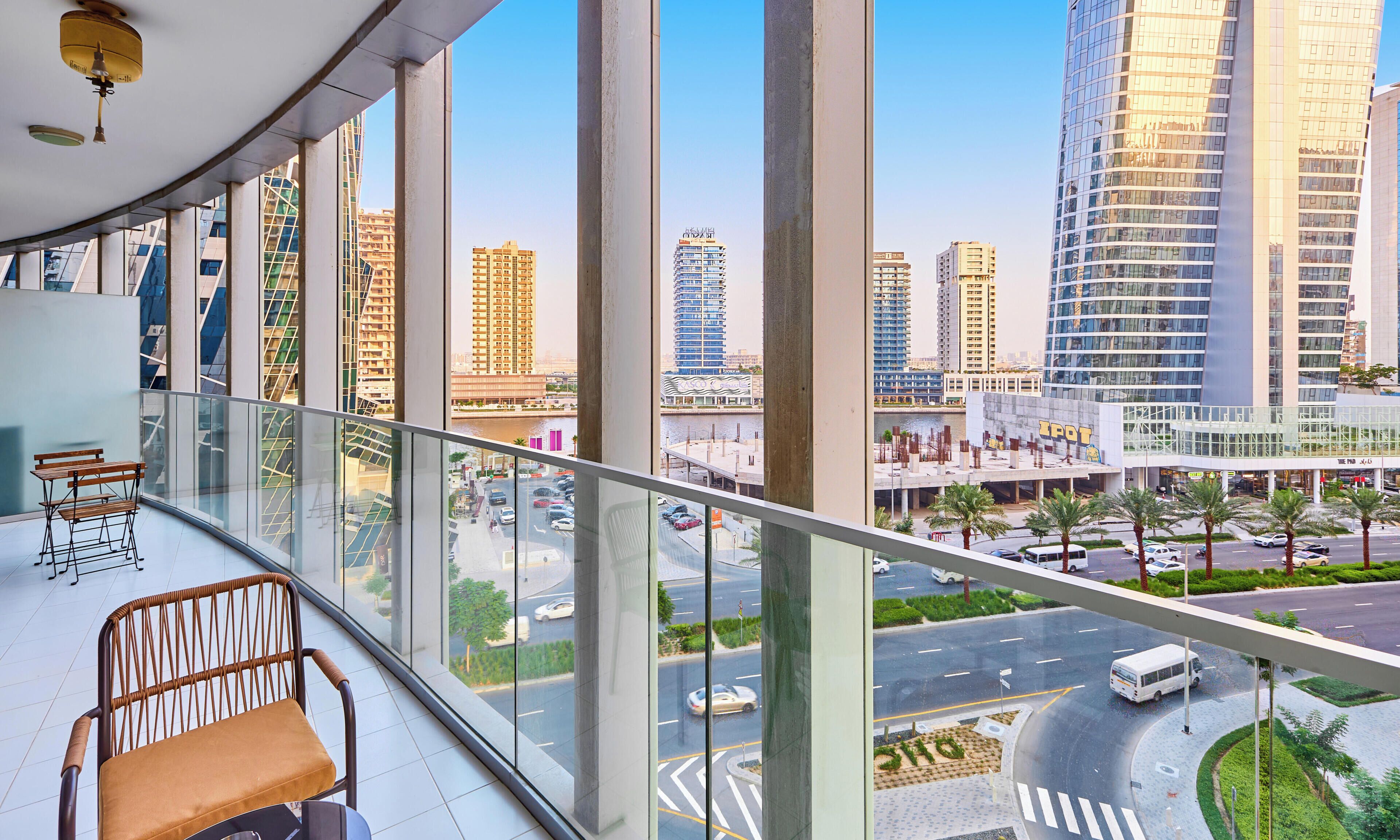 A balcony with a view of a cityscape, including high-rise buildings and a road with vehicles.