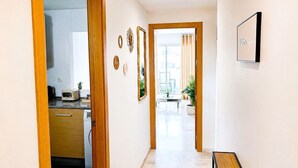 A hallway with a wooden door leading to a kitchen, a dining area with a table and chairs, and a view through a glass door. - Family apartment with sea views in Mijas Costa (Sitio de Calahonda)