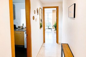A hallway with a wooden door leading to a kitchen, a dining area with a table and chairs, and a view through a glass door. - Family apartment with sea views in Mijas Costa (Sitio de Calahonda)