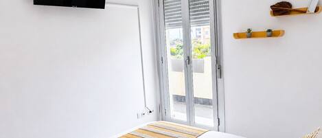 Une chambre à coucher comprenant un lit, un téléviseur fixé au mur, une porte coulissante donnant sur l’extérieur et une petite étagère ornée d’objets décoratifs.