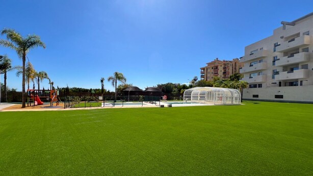 A hotel courtyard with a green lawn, a children's play area, and a transparent greenhouse structure. - Family apartment with sea views in Mijas Costa (Sitio de Calahonda)