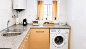 A compact kitchen with a built-in washing machine, a sink, and a window with curtains. - Family apartment with sea views in Mijas Costa (Sitio de Calahonda)