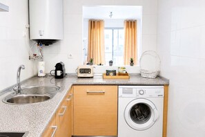 A compact kitchen with a built-in washing machine, a sink, and a window with curtains. - Family apartment with sea views in Mijas Costa (Sitio de Calahonda)