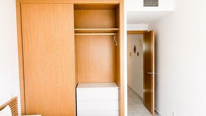 A bedroom with a wooden wardrobe, a white bedside table, and a bed with a striped blanket. - Family apartment with sea views in Mijas Costa (Sitio de Calahonda)