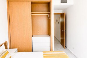 A bedroom with a wooden wardrobe, a white bedside table, and a bed with a striped blanket. - Family apartment with sea views in Mijas Costa (Sitio de Calahonda)