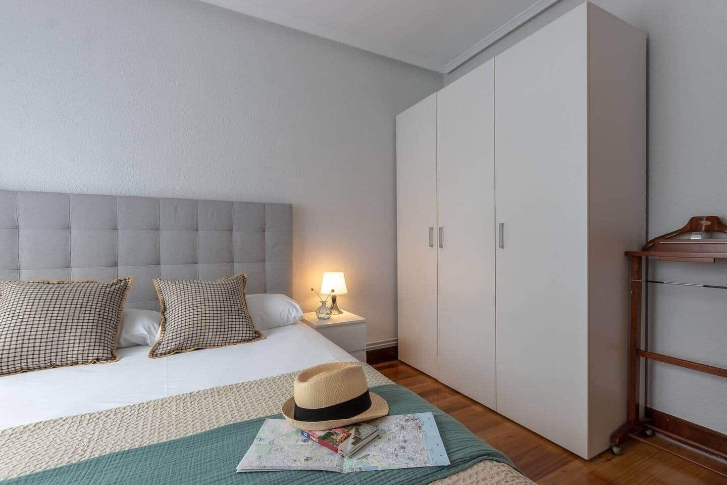 A hotel room with a bed, a nightstand, a lamp, a wardrobe, and a wooden hanger rack.