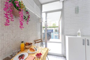 Ein Essbereich mit einem Tisch für zwei Personen, einem Korbwägelchen mit Blumen und Blick durch eine Glastür.