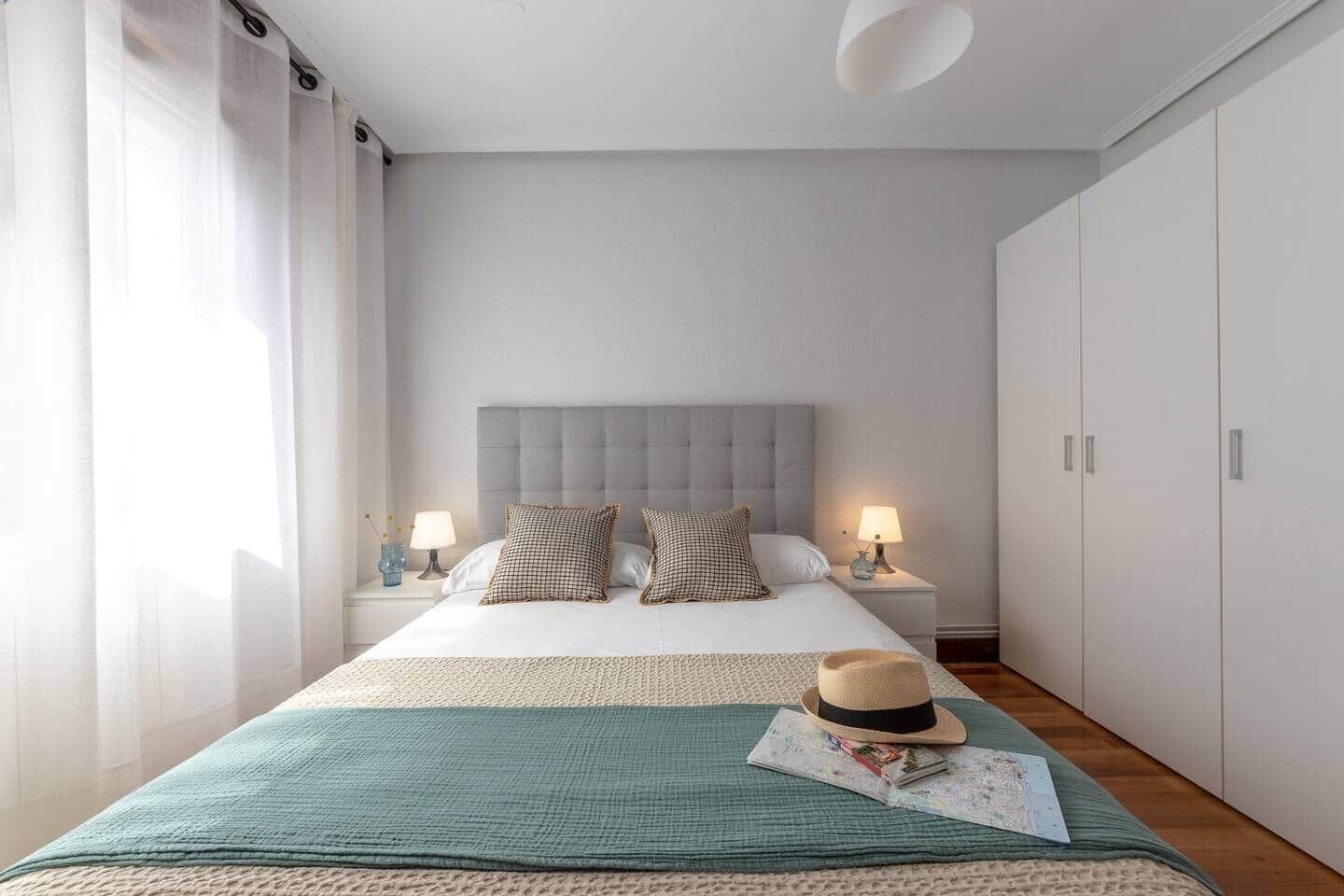 A bedroom with a bed, two nightstands, a wardrobe, and a window with curtains.