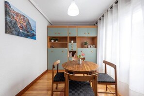 A dining area with a round wooden table, two chairs, a hanging light fixture, and a bookshelf with a 'HOME' sign. - POLITTE_Old Town vibes & parking (Bilbao)