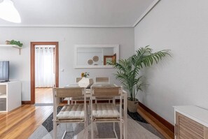 Un salon moderne avec un coin repas, comprenant un canapé, un téléviseur, une table à manger, des chaises, une plante en pot et un miroir décoratif.