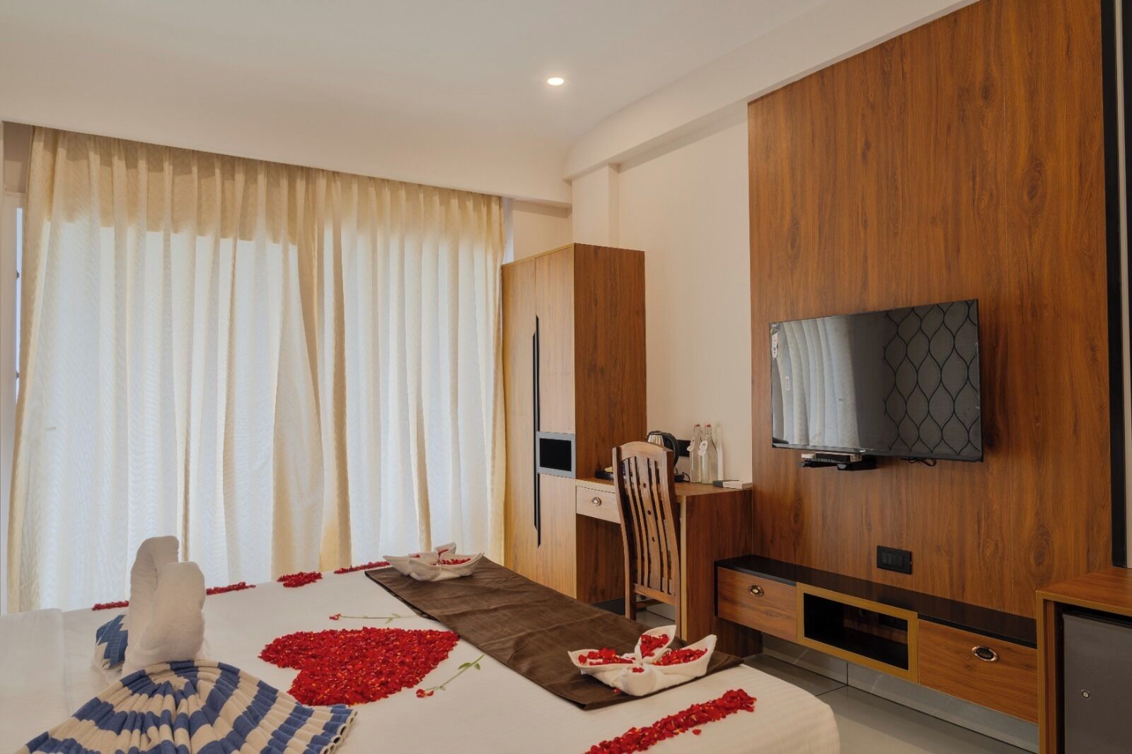 Una habitación de hotel moderna con una cama, un televisor montado en la pared, un armario de madera y un escritorio con una silla.