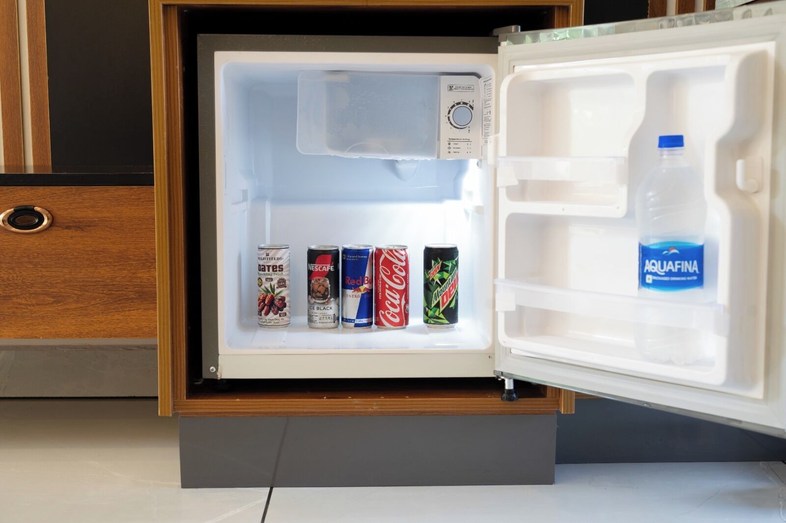 An open refrigerator with a water bottle and four beverage cans.