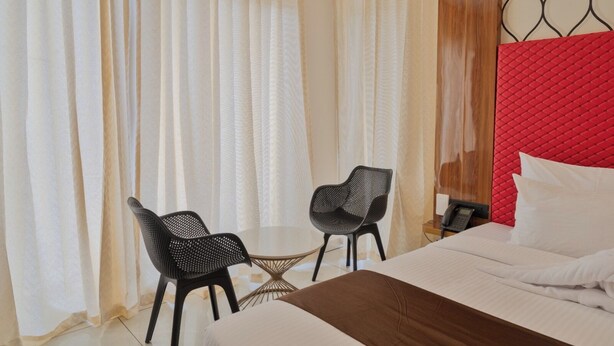 Habitación de hotel con cama, dos sillas, una mesita y un cabecero rojo.