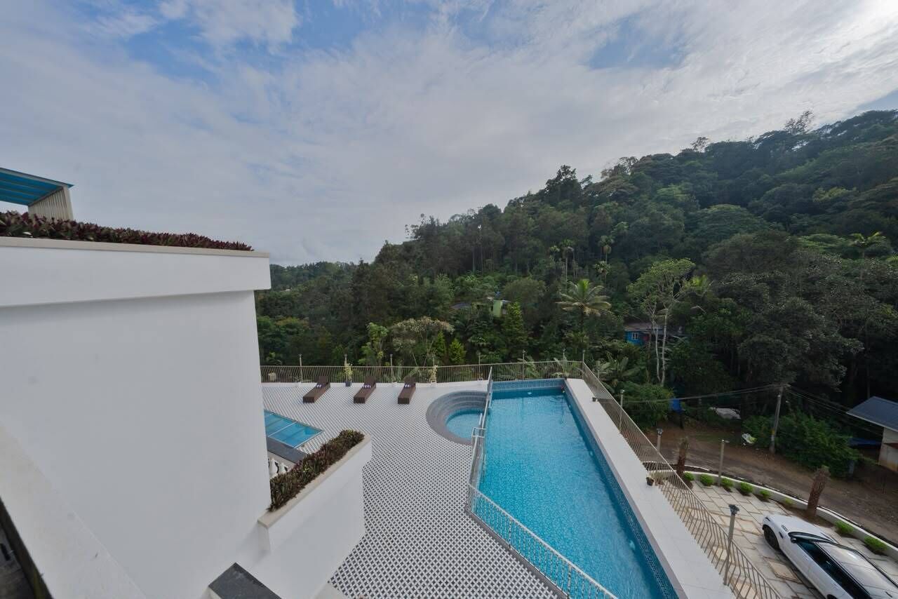 Una piscina en la azotea con sillones de descanso, rodeada de exuberante vegetación y un paisaje montañoso.
