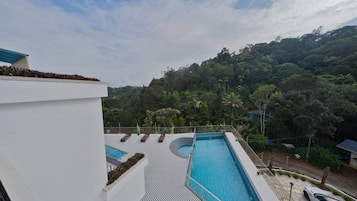 Una piscina en la azotea con sillones de descanso, rodeada de exuberante vegetación y un paisaje montañoso.