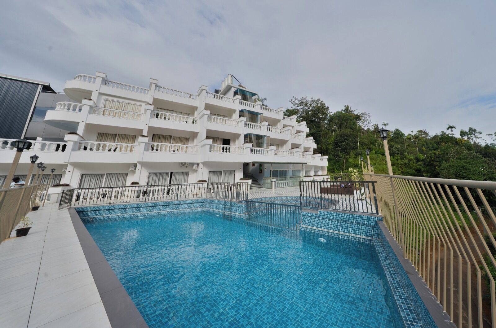 Un hotel moderno con piscina, varios balcones y vistas al entorno verde.