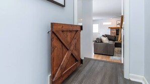 Um corredor com uma porta de madeira estilo celeiro, carpete cinza e uma sala de estar com um sofá cinza e uma lareira de tijolos ao fundo.