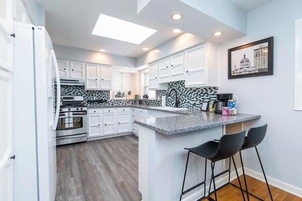 A modern kitchen with white cabinetry, a granite countertop, and a black and white backsplash.