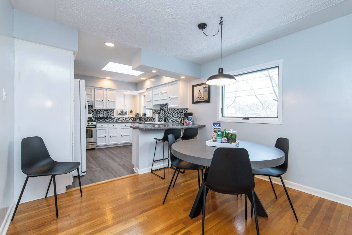 A modern kitchen with white cabinets, a central island, and a dining area with a round table and four chairs.
