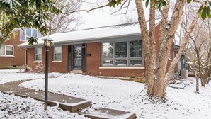 Uma casa residencial com fachada de tijolos, varanda frontal e quintal coberto de neve.