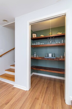 A staircase with wooden steps leading to a room with a green wall and wooden shelves holding glassware and decorative items.