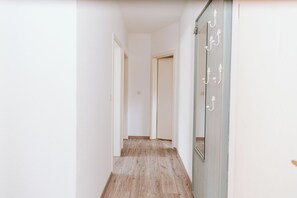 Ein Korridor mit Holzboden und weißen Wänden, der zu einer Tür mit Spiegel und Wandhaken führt.