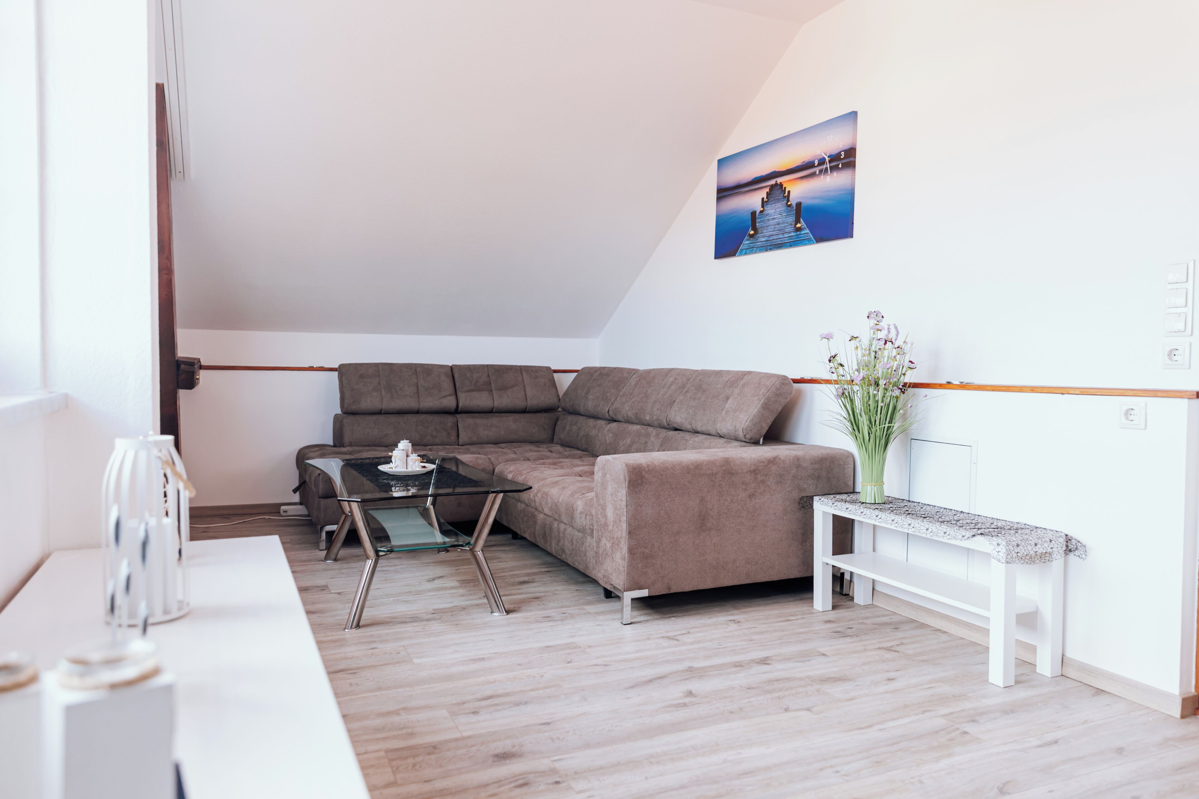 A modern living room with a sectional sofa, a glass coffee table, and a white side table with a vase of flowers.