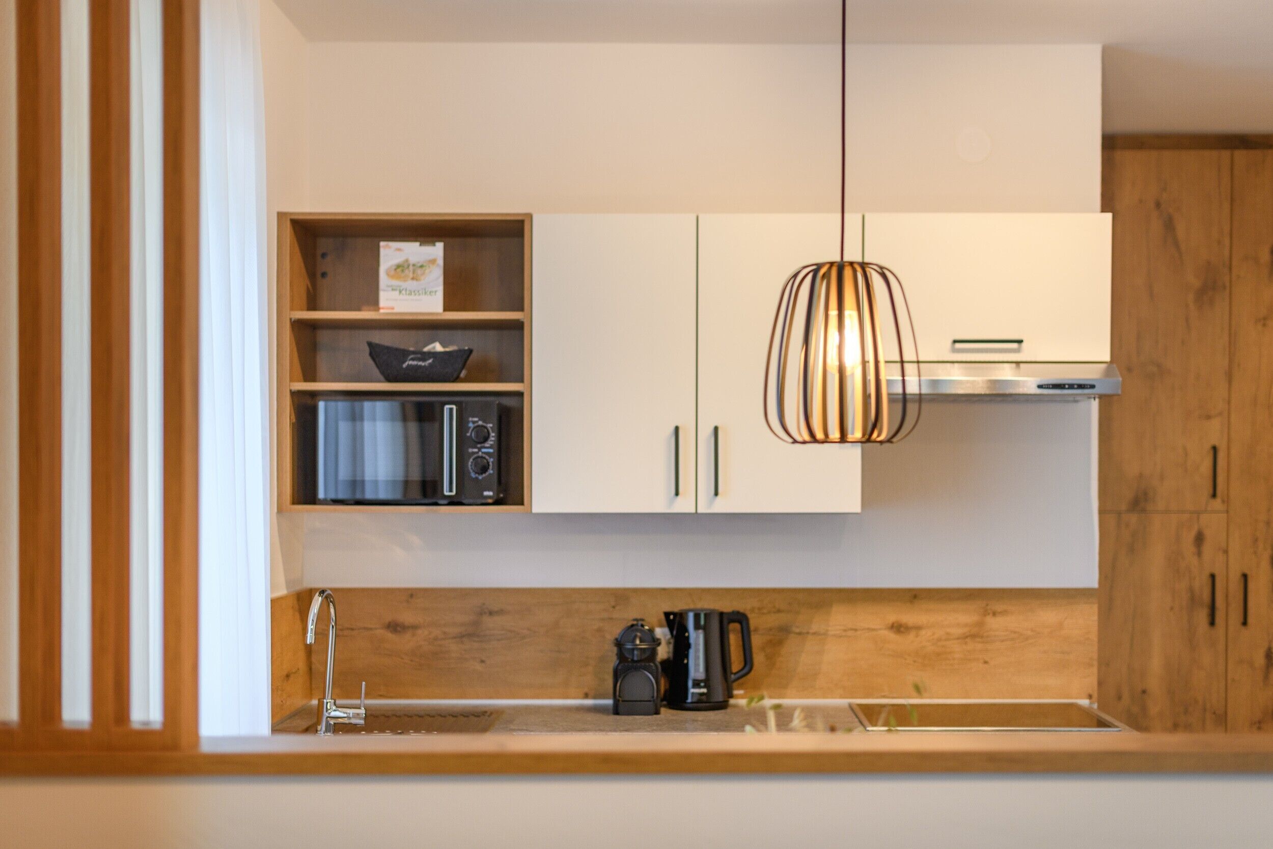 Une cuisine moderne avec des meubles en bois, un four à micro-ondes encastré et un luminaire suspendu.