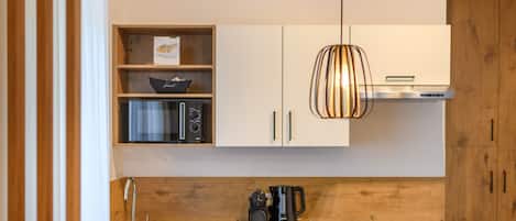 Una cocina moderna con gabinetes de madera, microondas integrado y una lámpara colgante.