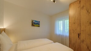A bedroom with two beds, a wooden wardrobe, and a painting on the wall.