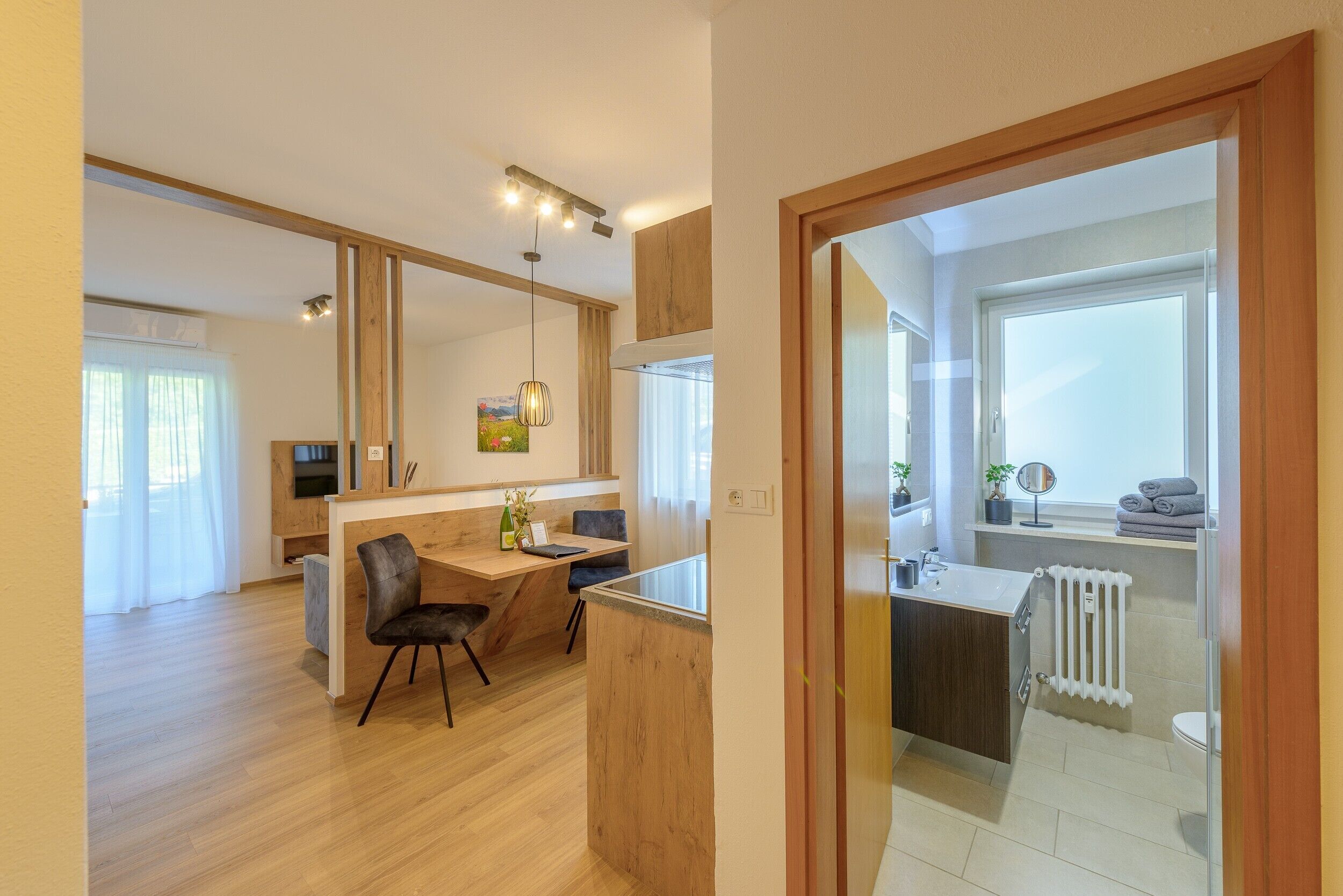 Une cuisine moderne avec des meubles en bois, un coin repas avec une table et des chaises, et une vue sur le salon grâce à une porte ouverte.