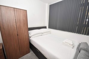 A bedroom with a bed, a wardrobe, and a window with blinds. - Modern Studio Apartment in Central Bradford (Bradford)