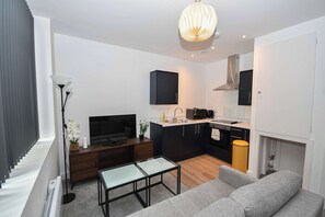A modern living room with a flat-screen TV, a sofa, a glass coffee table, and a dining area with a microwave. - Modern Studio Apartment in Central Bradford (Bradford)