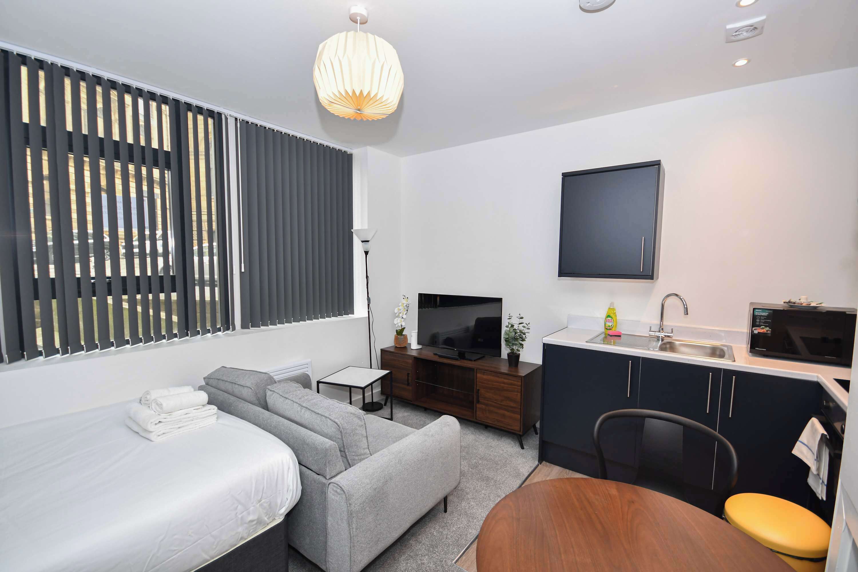 Une chambre à coucher moderne avec un lit, un canapé gris et un téléviseur.