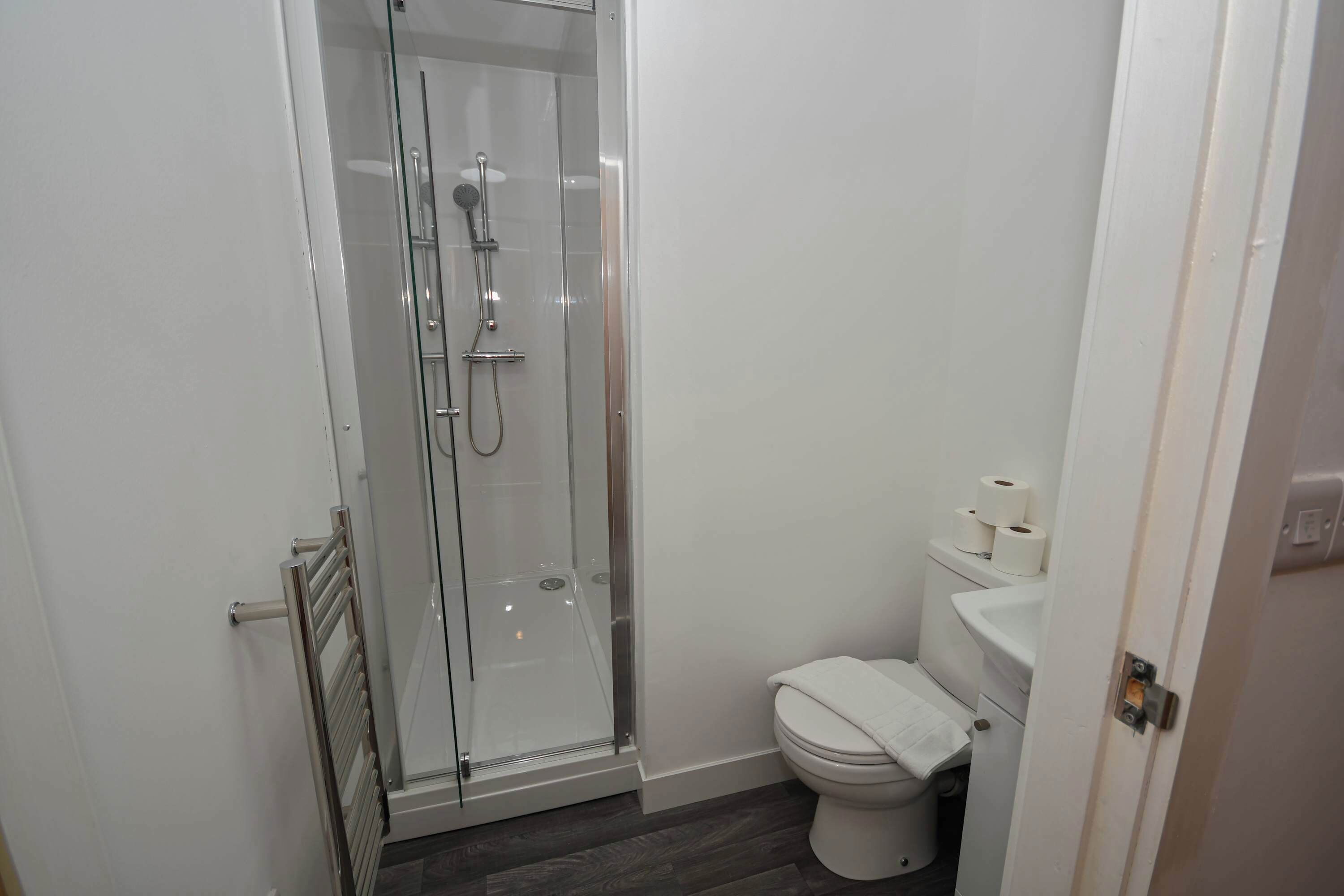 A bathroom with a glass-enclosed shower, a toilet, and a towel rack.