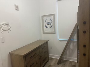 Een kamer met een houten dressoir, een kunstwerk met een krab in een lijst en een raam met jaloezieën.
