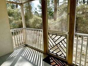 Ein sonnendurchflutetes Zimmer mit Blick auf Bäume durch ein Fenster, eine Holztür und ein Fliesenboden.