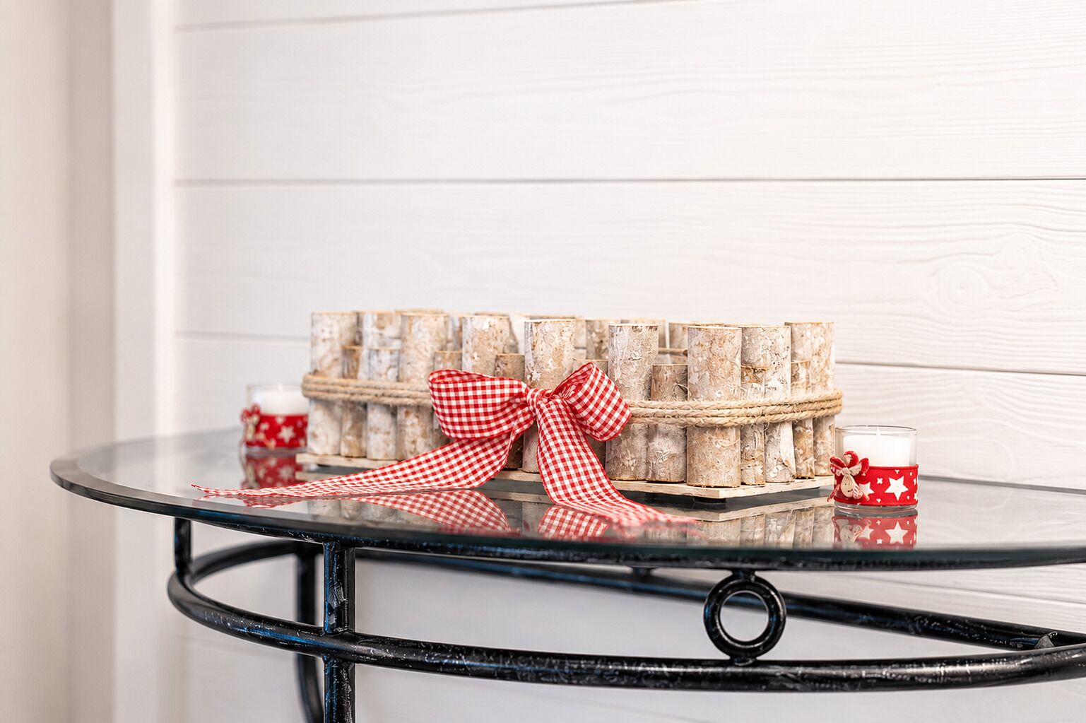 A glass table with a metal frame, a decorative box with a red bow, and two small candle holders with red and white patterns.