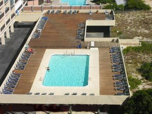 An aerial view of a rooftop pool area with a square pool surrounded by lounge chairs and a wooden deck. - Enjoy beautiful oceanfront views of the Ocean City coastline in this one bedroom, one bath condo located just a few steps from the beach! (Ocean City)